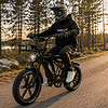 Kypäräpäinen mies ajaa sähköpyörällä metsätiellä auringonlaskussa.